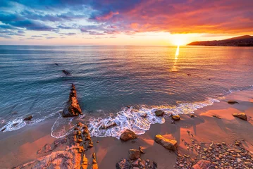 Foto auf Glas Sanremo, Riviera dei Fiori, Liguria, Italy. Scenis rocks and pebbles on beach illuminated beautiful by sunset light. Dramatic colourful sky waving sea. © fabio lamanna