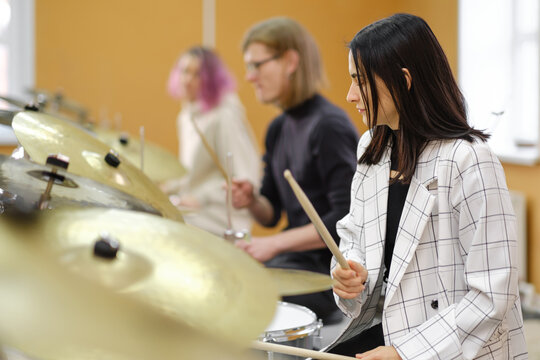 Young adult men and women learn to play drums at school. Hobbies and pastime.