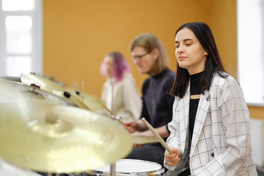 Young adult men and women learn to play drums at school. Hobbies and pastime.