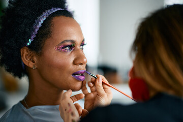 Black woman putting on colorful make-up for Mardi Gras festival celebration.