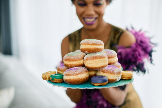 Close-up of woman with plate of donuts sprinkled with traditional Mardi Gras colors.