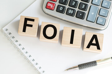 FOIA text on wooden cubes on the background of a white notepad next to the calculator and pen on the table