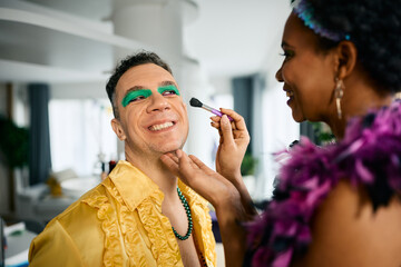 Happy man has fun while his friend is putting him Mardi Gras make-up for festival celebration.