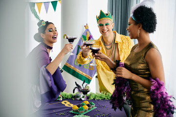 Multiracial group of friends celebrating Mardi Gras and toasting with drinks at home party.