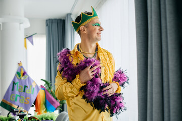 Happy gay man wears carnival costume during Mardi Gras festival and looks through the window.