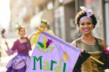 Happy African American woman holds Mardi Gras flag during the carnival.
