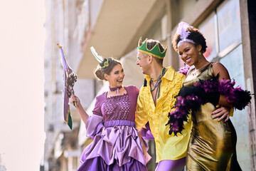 Multi-ethnic group of people in costumes celebrating and having fun on Mardi Gras street carnival. - obrazy, fototapety, plakaty