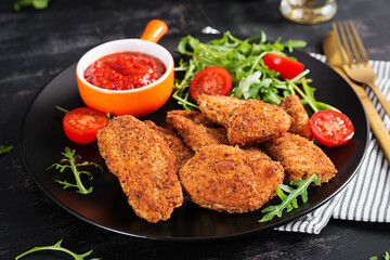 Chicken nuggets and sauce in black plate on a dark background.