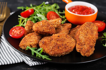 Chicken nuggets and sauce in black plate on a dark background.