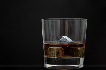 Gray whiskey soapstonestones in the glass. Close up view of whisky stones in the glass with whisky isolated on dark background whith copyspace
