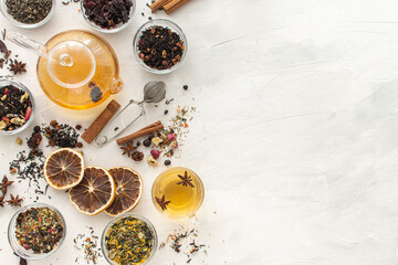 Several varieties of herbal and fruit tea in glass bowls and a kettle with a cup of hot tea on a light background. View from above. Healthy eating. Delicious warming drink. Copy spase