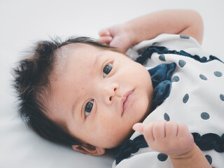 Portrait of three weeks Australian Asian newborn baby or infant lying on the white bed and opening her eyes..