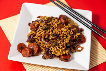 Um prato branco com uma porção de yakisoba de legumes com molho de soja. Yakisoba vegetariano dentro de um prato sobre a superfície vermelha.