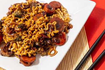 Um prato branco com uma porção de yakisoba de legumes com molho de soja. Yakisoba vegetariano dentro de um prato sobre a superfície vermelha.