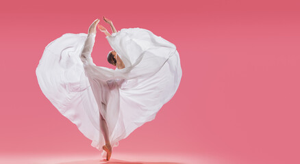slender graceful ballerina in pointe shoes waves a long white skirt showing a heart shape on a pink background