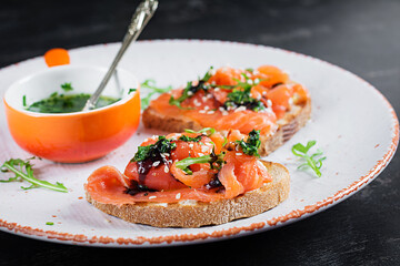 Healthy toasts with salmon, cream cheese,  sesame seeds, black pepper and arugula on plate.