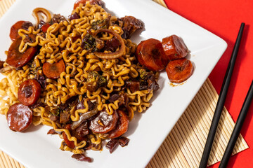 Um prato branco com uma porção de yakisoba de legumes com molho de soja. Yakisoba vegetariano dentro de um prato sobre a superfície vermelha.