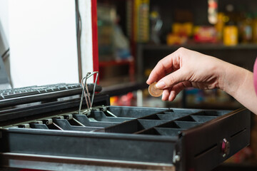 latina woman's hand taking money from the cash register, making a sale in her grocery store, girl...