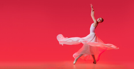 elegant ballerina in pointe shoes dancing in a long white skirt on a red background © Maria Moroz