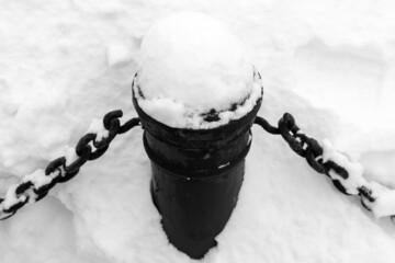 Black iron fence pillar with chains is covered with snow