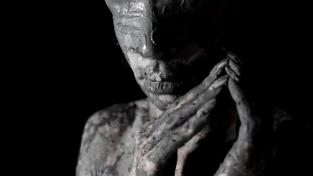 blindfolded woman and covered by clay is standing in dark room, closeup of face and hands
