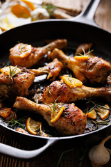 Roasted chicken legs, drumsticks with rosemary, garlic and lemon in a cast iron skillet, close up view