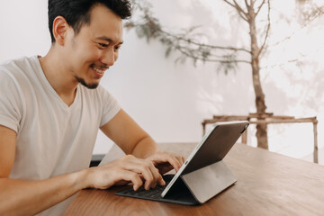 Happy freelance Asian man working with his tablet in the cafe.