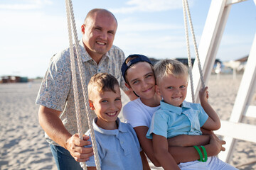 Happy father swings his sons on a swing by the sea. Big family on vacation on the coast in summer
