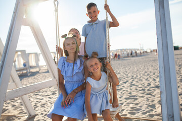 Happy mom, two daughters and son are swinging on a swing by the sea