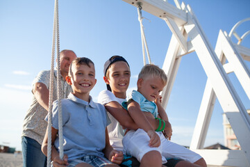Happy father swings his sons on a swing by the sea. Big family on vacation on the coast in summer