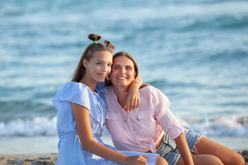Mom and her teenage daughter hugging and smiling together over blue sea view