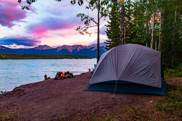 perfect camping spot on Abraham lake at sunset with bright sky, tent and fire 