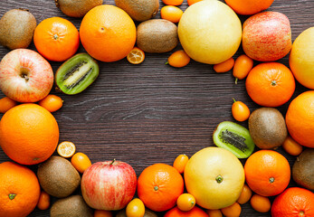 Flat lay view of various fruits frame background. Room for text in the center. Lot of different fruits: kiwis, kumquats, apples, tangerines, oranges, pomelos.