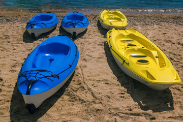 Bright blue and yellow kayak boats on a beach near sea water. Canoe for summer activity.  - Powered by Adobe