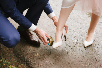 A young guy in a suit (groom) cleans dirty shoes on the girl's (bride) leg