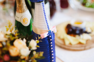 A bottle of champagne decorated as a groom at a wedding, flowers and food on the background