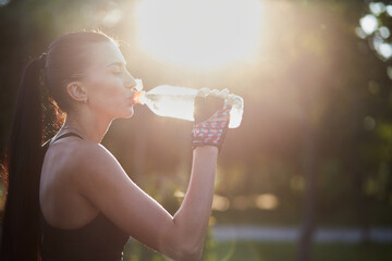 Girl athlete with a bottle in his hands drinks water while exercising in the park