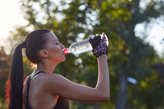 Girl athlete with a bottle in his hands drinks water while exercising in the park