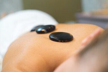 spa therapist is placing hot stone on women back