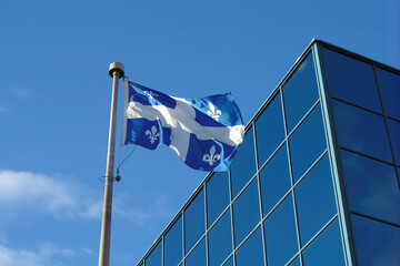Naklejka premium Quebec, Canada, Montreal north america french culture flag fluttering in the wind blue glass building