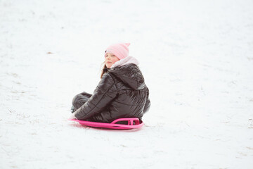 Happy little girl sliding down the hill on saucer sled. Girl enjoying slider ride on the snow