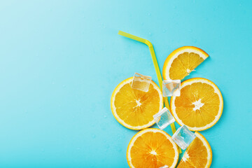 Orange slices and ice cubes with a straw on a blue background in the shape of a cocktail.