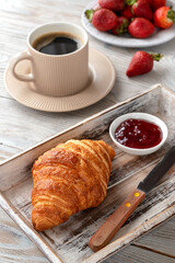 Croissant with strawberry jam, strawberries and a cup of coffee for breakfast.