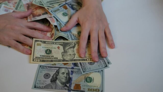 Women's hands take a pile of paper money with American one hundred dollar bills, ten dollar bills and Russian five thousandth bills
