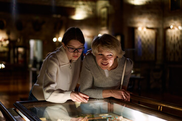 Girl with woman looking with interest at art objects under glass in museum