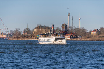 Old steam boat in the bay Saltsjön passing the island Djurgården and the ness Waldermars Udde a sunny winter day in Stockholm