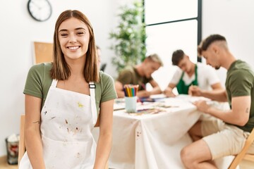 Young woman standing at art studio looking positive and happy standing and smiling with a confident smile showing teeth