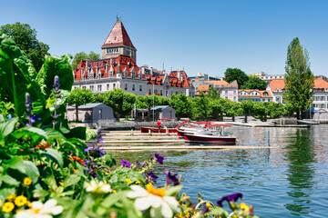 Chateau D'ouchy beside the Lake Leman with flowers in the foreground - Boats at the pier in the leisure area of ​​the city of Lausanne in Switzerland