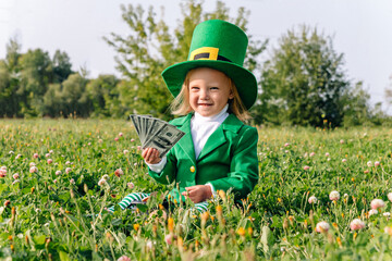 St. Patrick's Day holiday. A girl dressed in a Leprechaun costume sits in a clover meadow and holds...