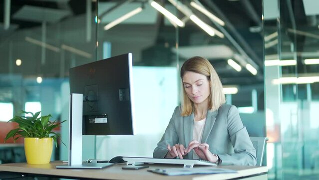 Female Office Worker In Suit Working At Computer Pc In Front Of Monitor Correspondence Sitting At Desk. Employee In A Modern Workplace. Blonde Woman Busy Entrepreneur Secretary Typing Text Message